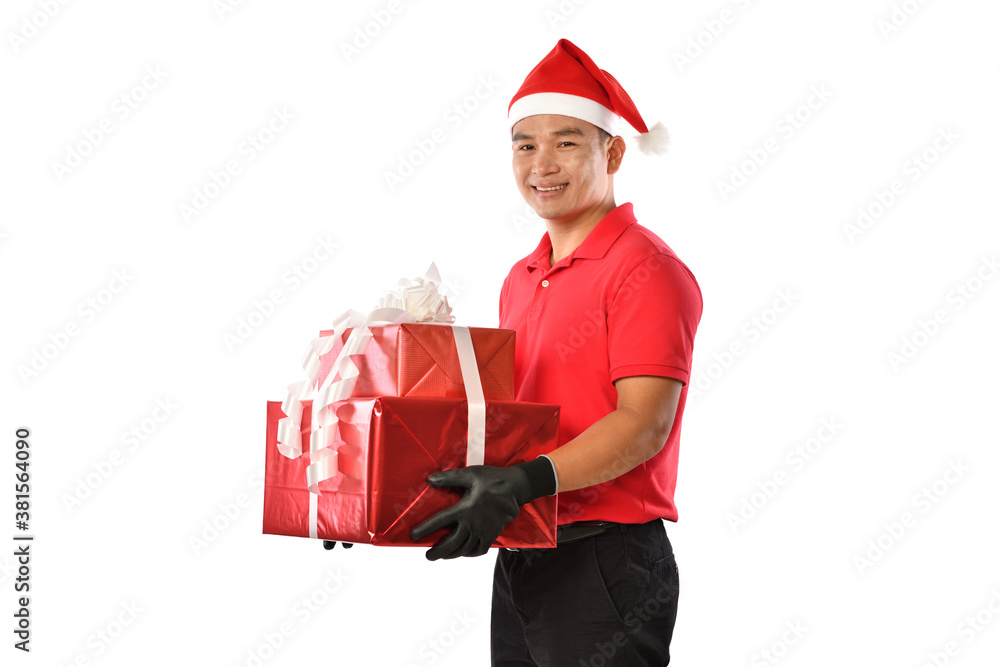 Happy young Asian delivery man in red uniform, Christmas hat carry boxes of presents in hands isolat