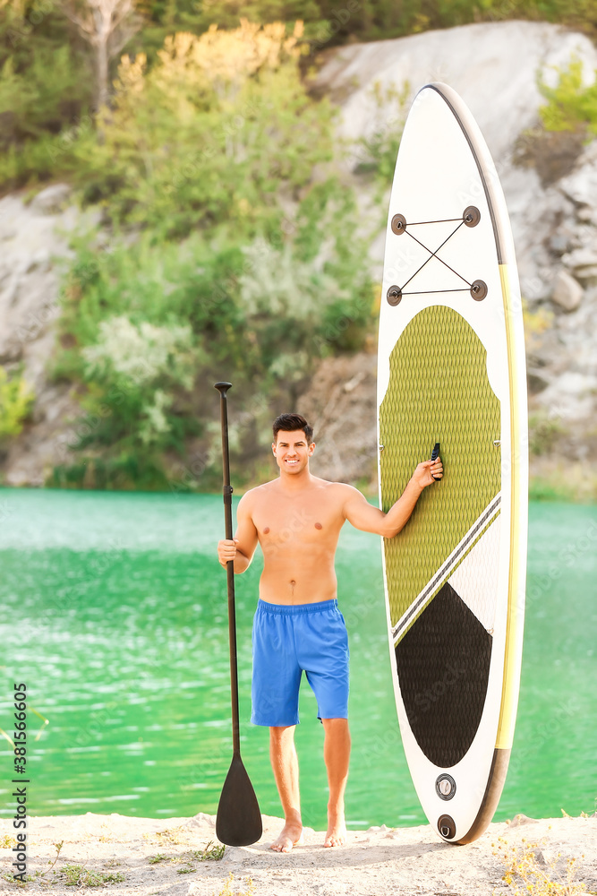 Young man with board and paddle for sup surfing near river