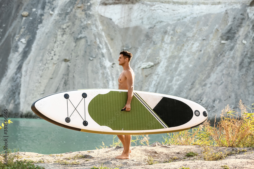 Young man with board for sup surfing near river