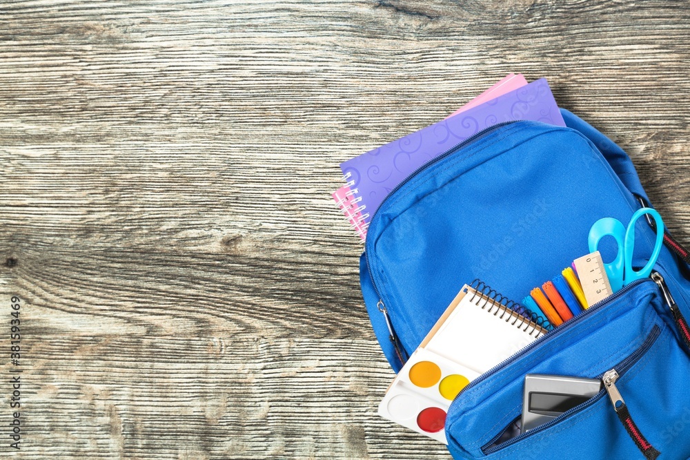 Classic school backpack with colorful school supplies and books on desk.