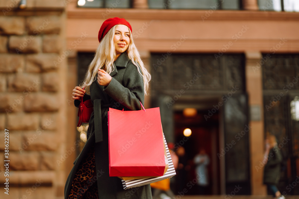 Portrait of young elegant woman wearing stylish red beret holding shopping bags in the city street. 