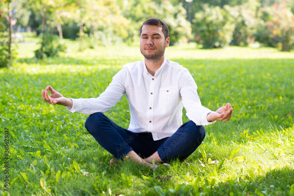 Young man meditates in lotus pose on green grass