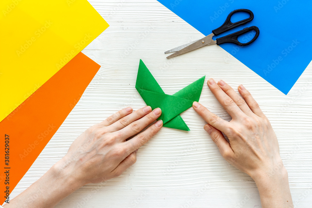 Female hands folding sheet of paper - origami bird. Overhead view