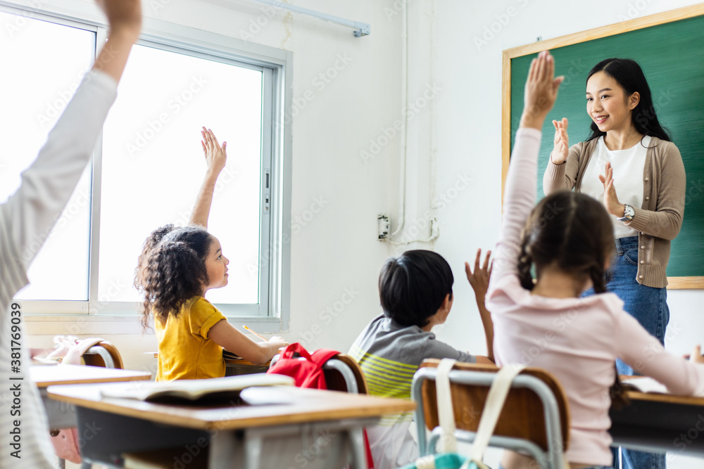 Diversity of elementary school students raise their hands to answer teacher questions. Back to schoo