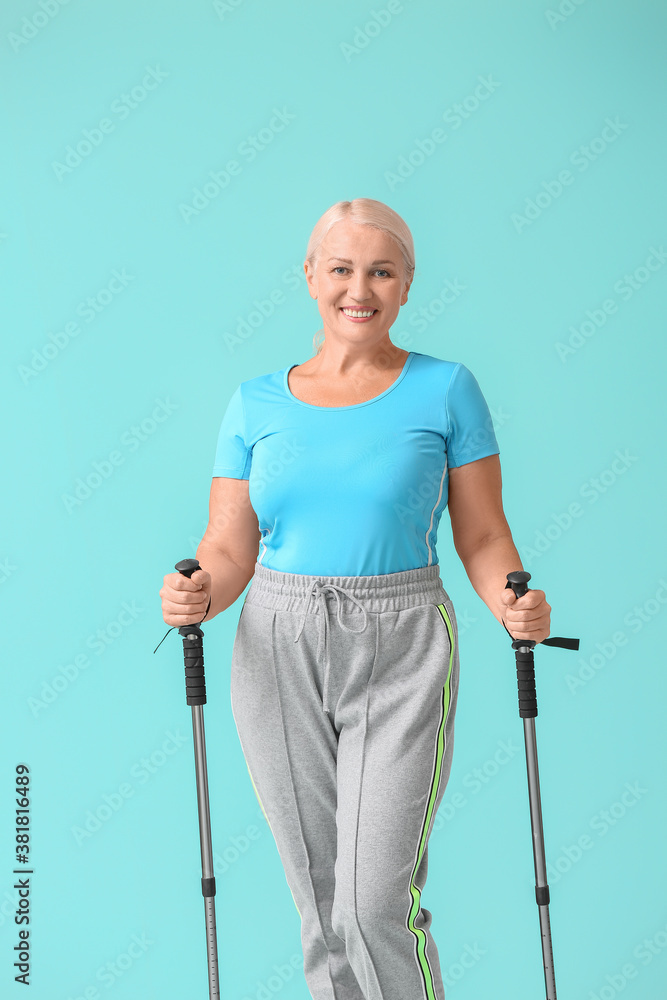 Mature woman with walking poles on color background