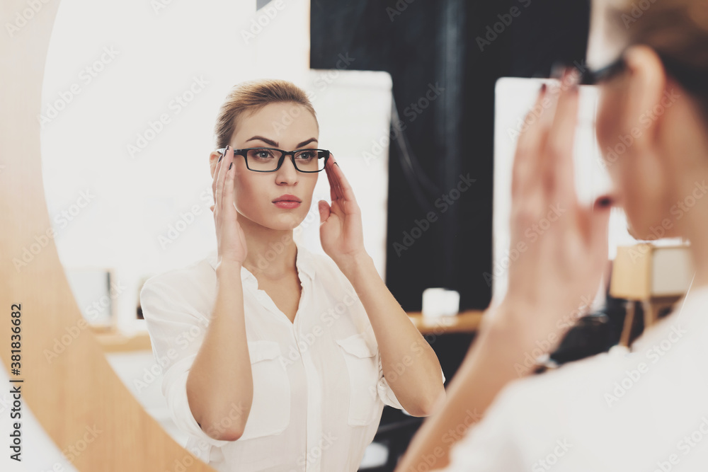 Woman looking in mirror and holding on to glasses.