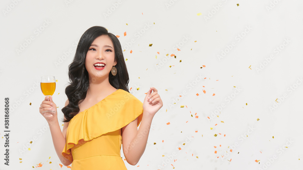 Gorgeous lady in yellow dress hold champagne, throwing confetti on white background.