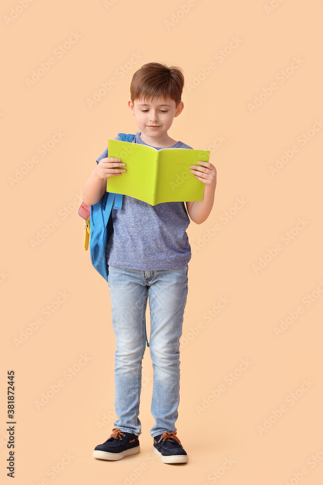 Little schoolboy with notebook on color background