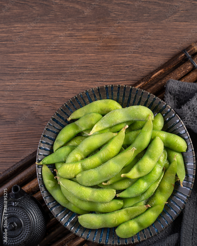 Fresh cooked boiled edamame in a plate on wooden tray and table background, healthy protein food con