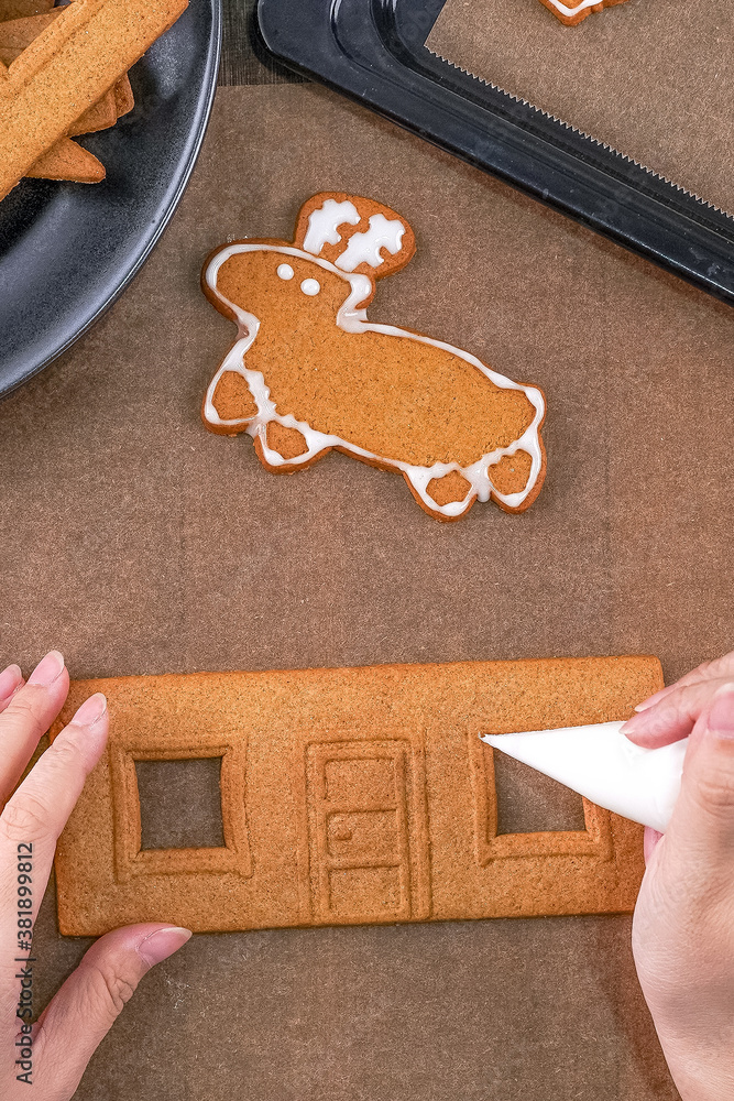 Young woman is decorating Christmas Gingerbread House cookies biscuit at home with frosting topping 