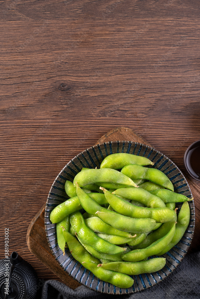 Fresh cooked boiled edamame in a plate on wooden tray and table background, healthy protein food con