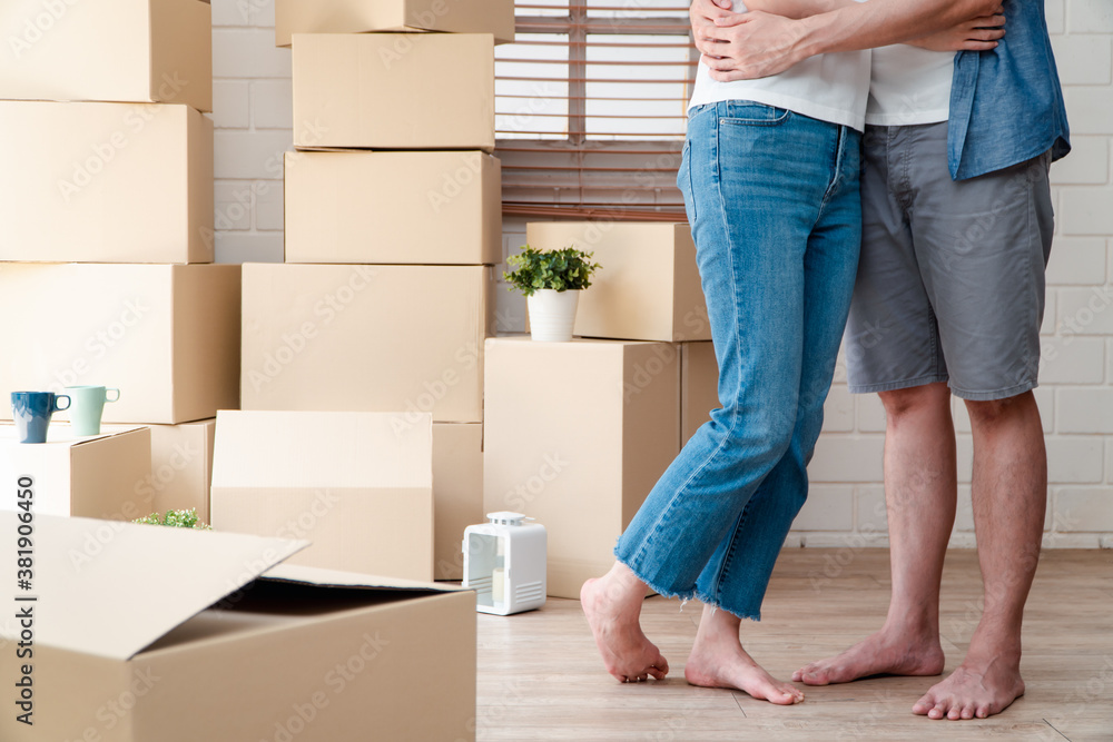 Smiling young Asian happy couple hugging boyfriend with cardboard boxes at moving day in their new h