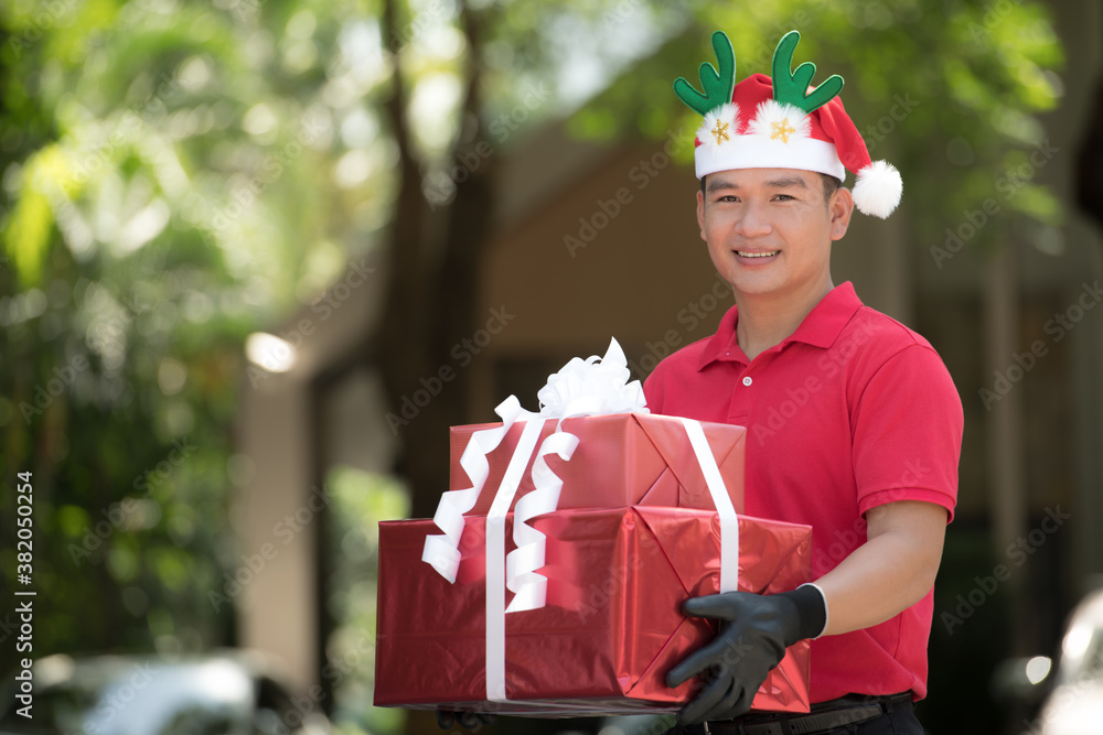 Asian delivery man in red uniform and Christmas hat delivering present and gift boxes to recipient f