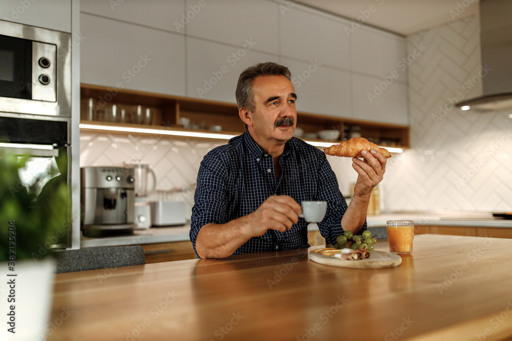 Eating his breakfast while holding and drinking coffee.