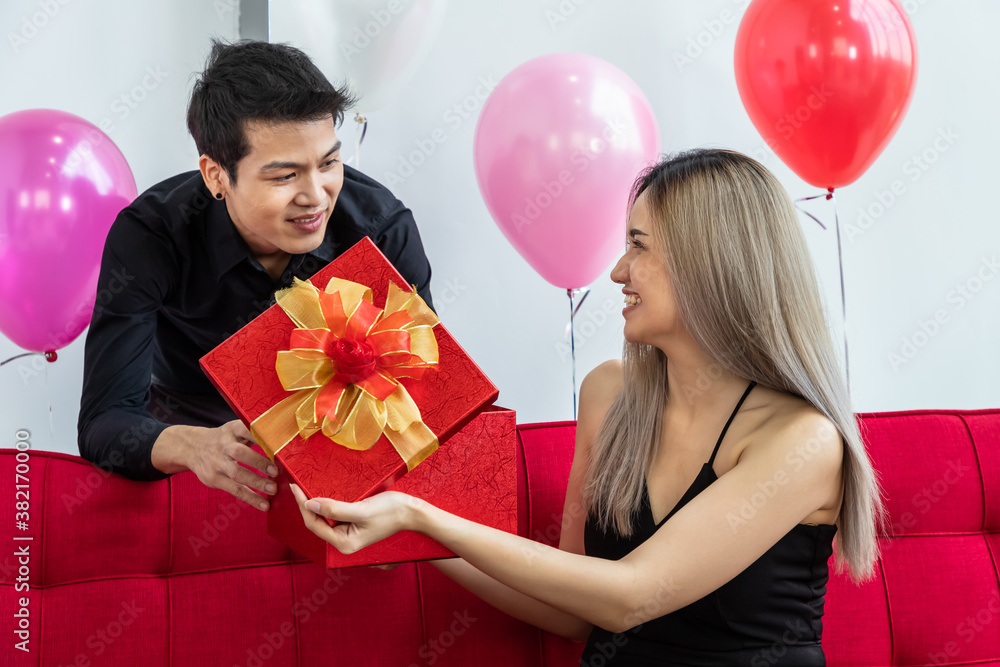 Attractive young couple celebrate anniversary, together. Man giving present gift box to woman.