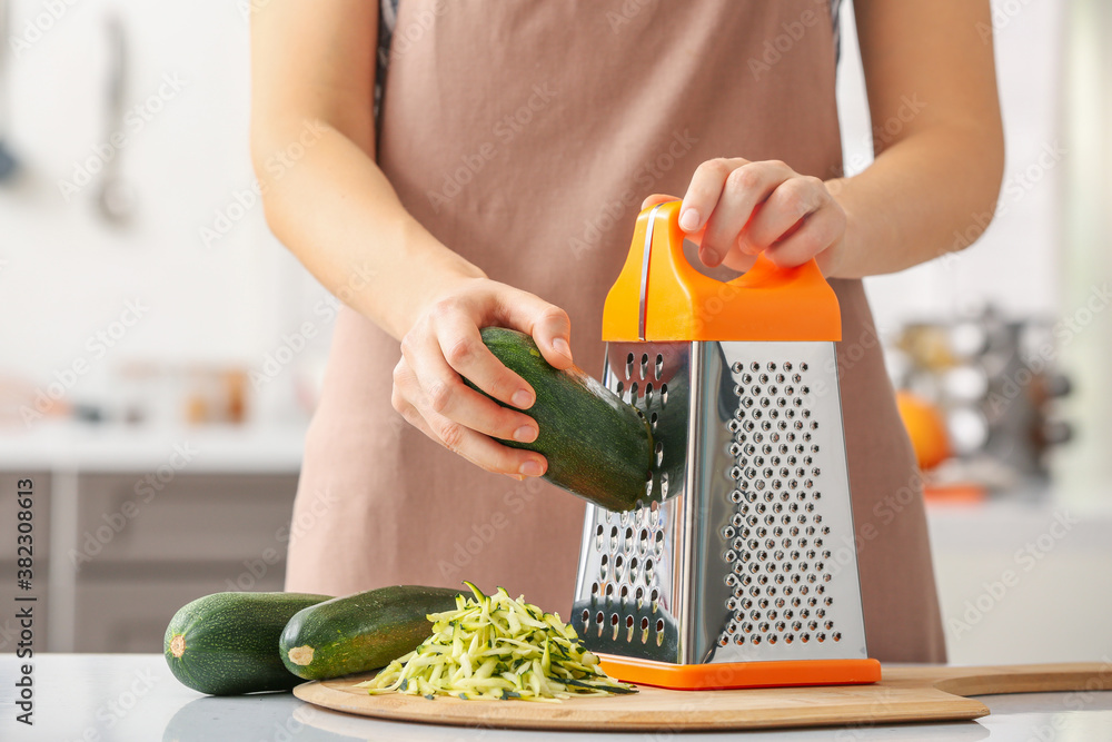 Woman grating zucchini in kitchen