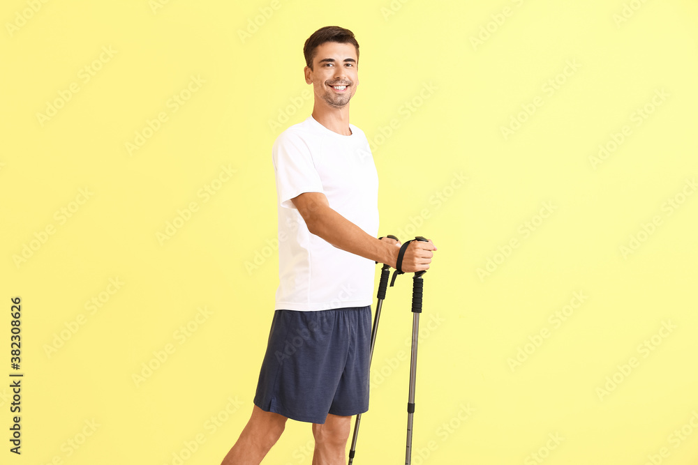 Young man with walking poles on color background