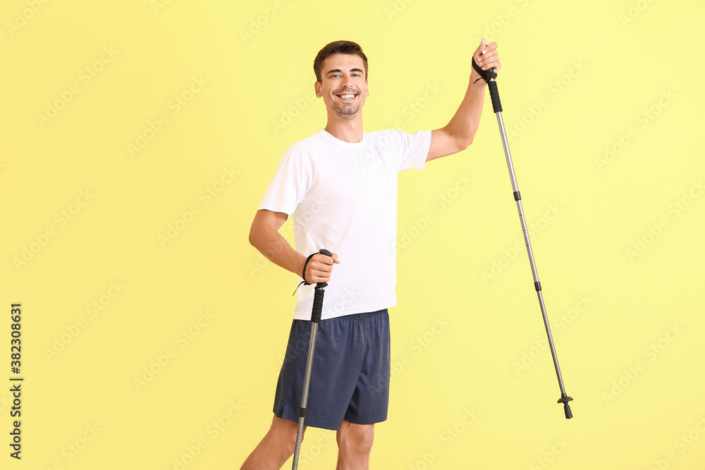 Young man with walking poles on color background