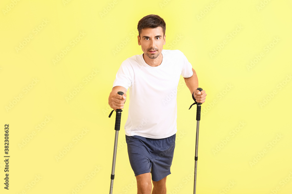 Young man with walking poles on color background