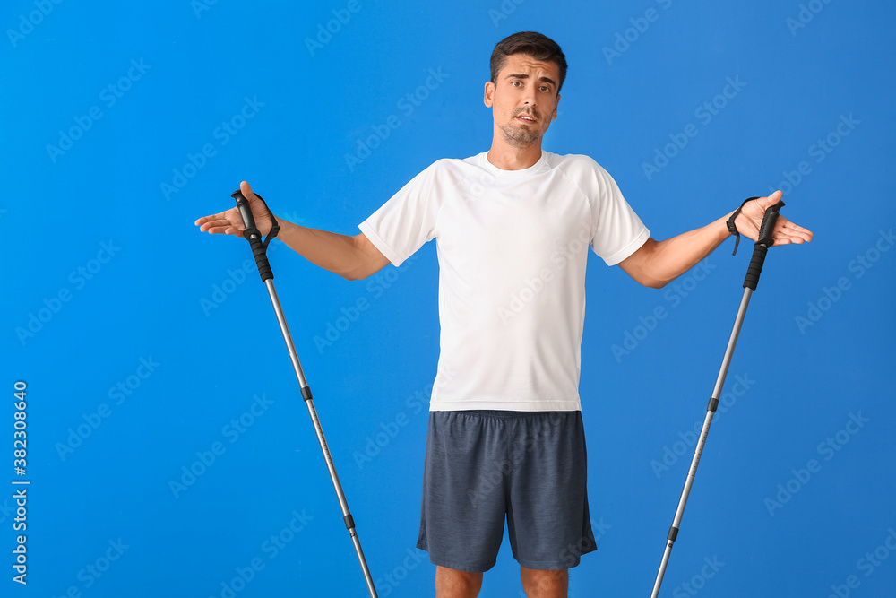 Confused young man with walking poles on color background