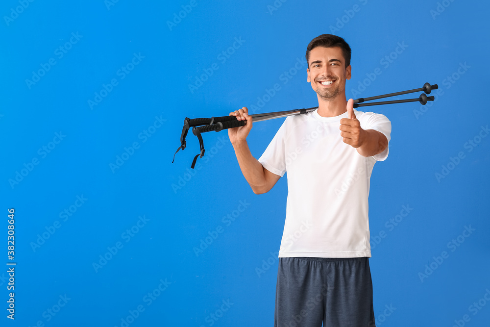 Young man with walking poles showing thumb-up on color background