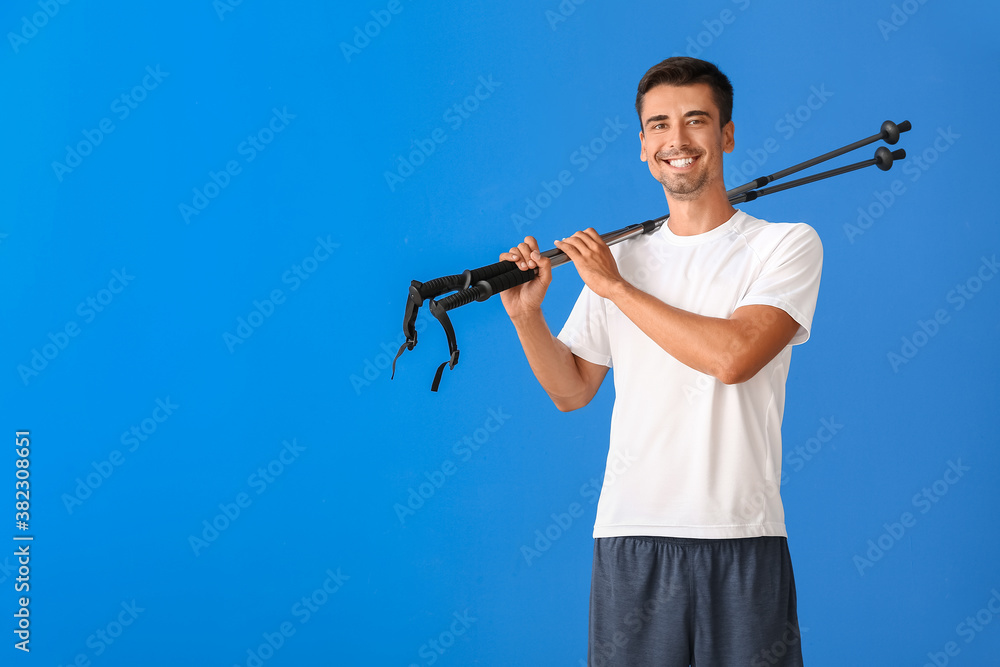 Young man with walking poles on color background