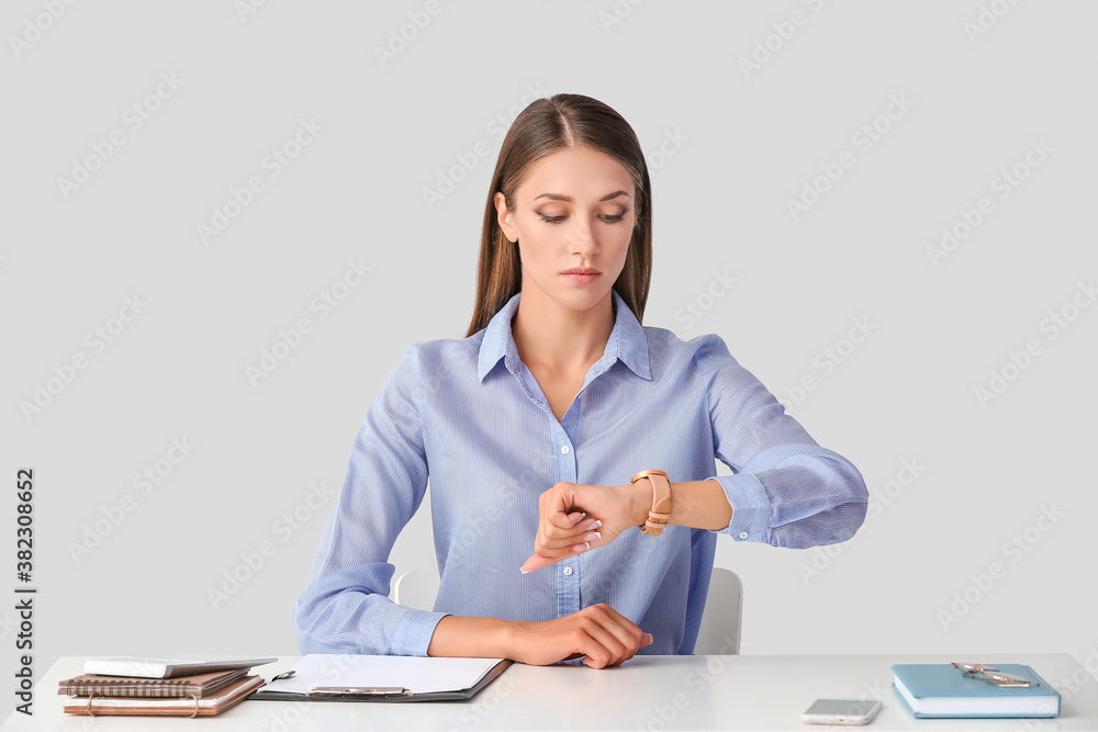 Young woman with wristwatch sitting at table on light background