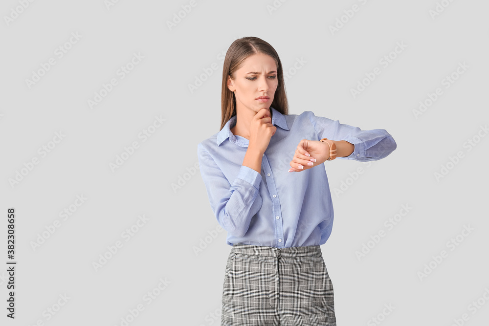 Thoughtful young woman with wristwatch on light background