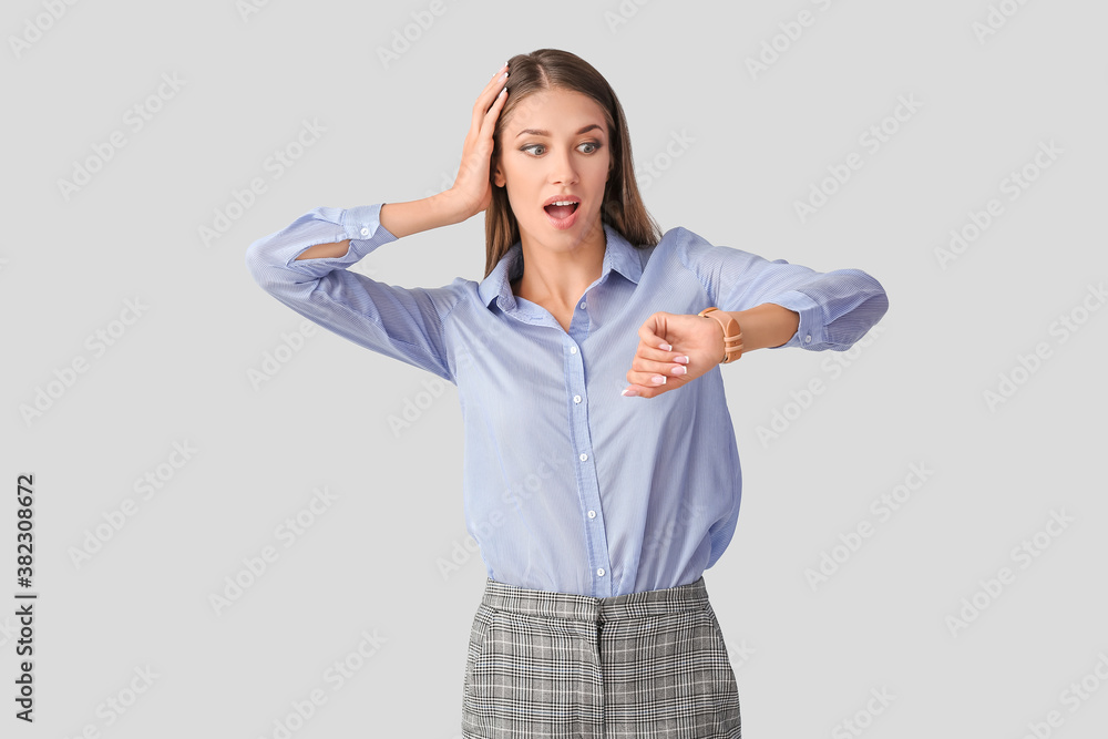 Shocked young woman with wristwatch on light background