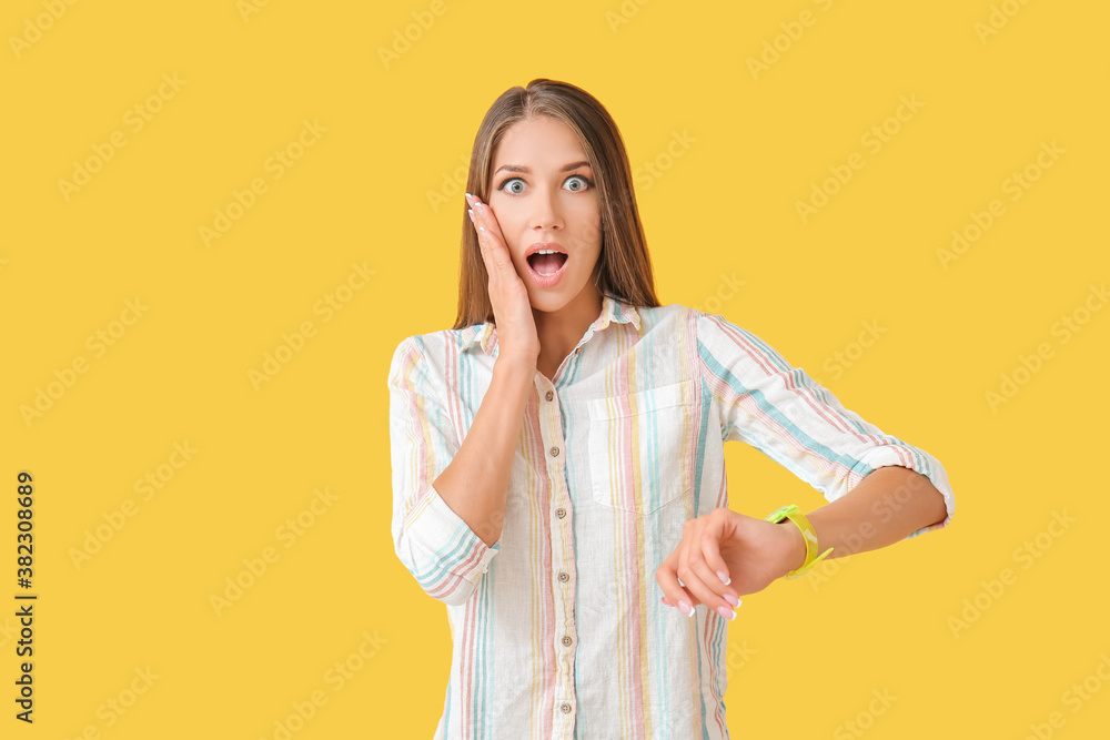 Shocked young woman with wristwatch on color background