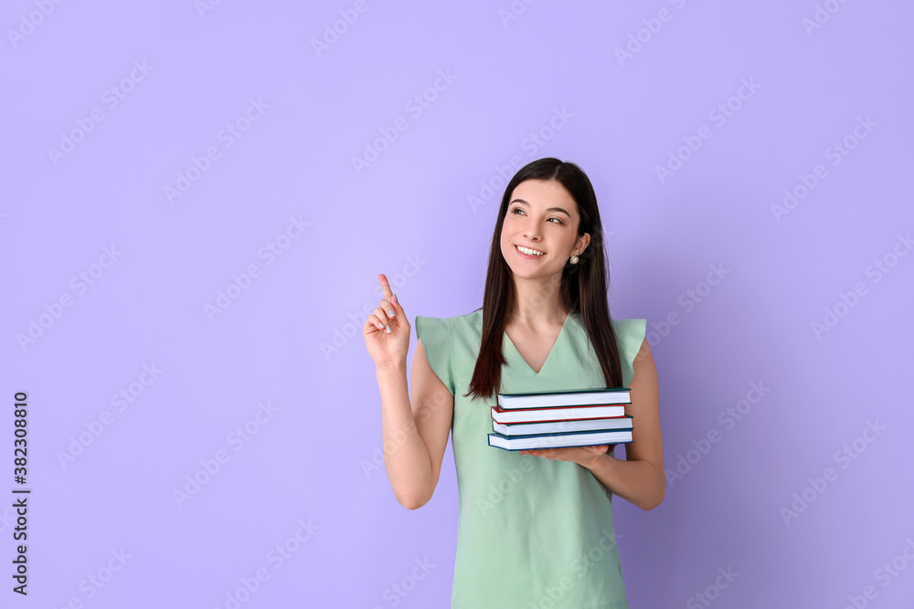 Beautiful young woman with books pointing at something on color background