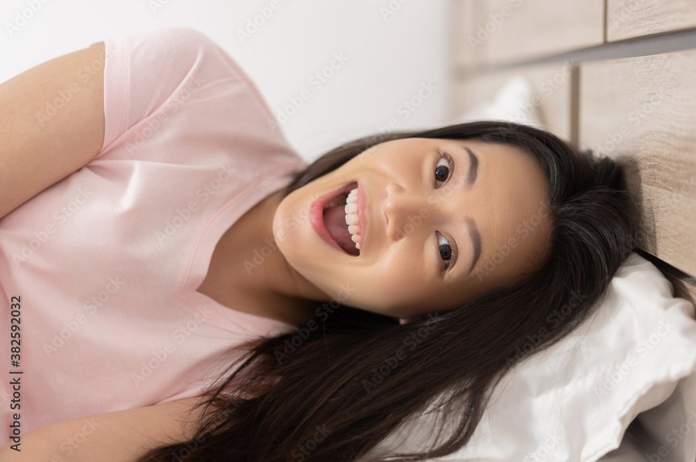 Asian woman poses with excitement and surprise in bed.