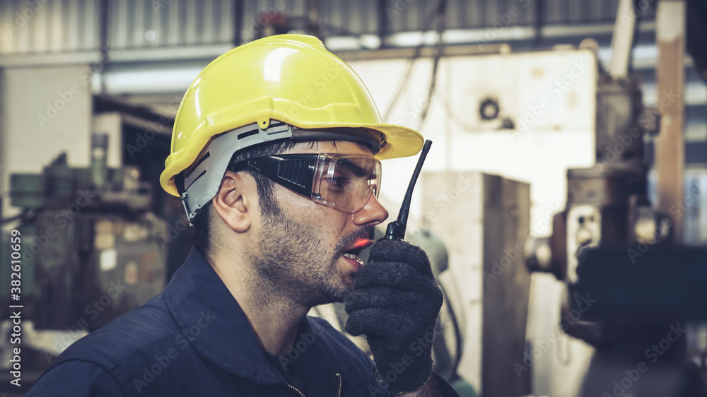 Factory worker talking on portable radio while inspecting machinery parts . Industrial and engineeri