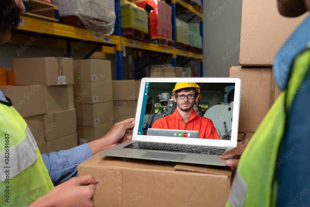 Warehouse staff talking on video call at computer screen in storage warehouse . Online software tech