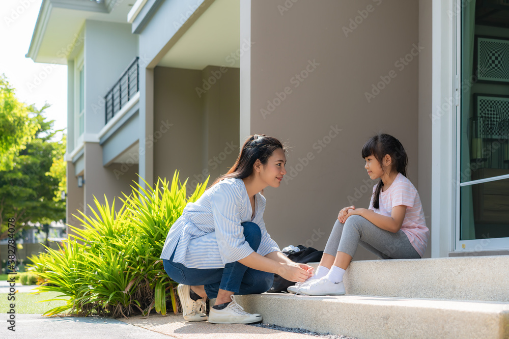 Asian mother help her daughter primary students in uniform to wearing their shoelace of shoes infron