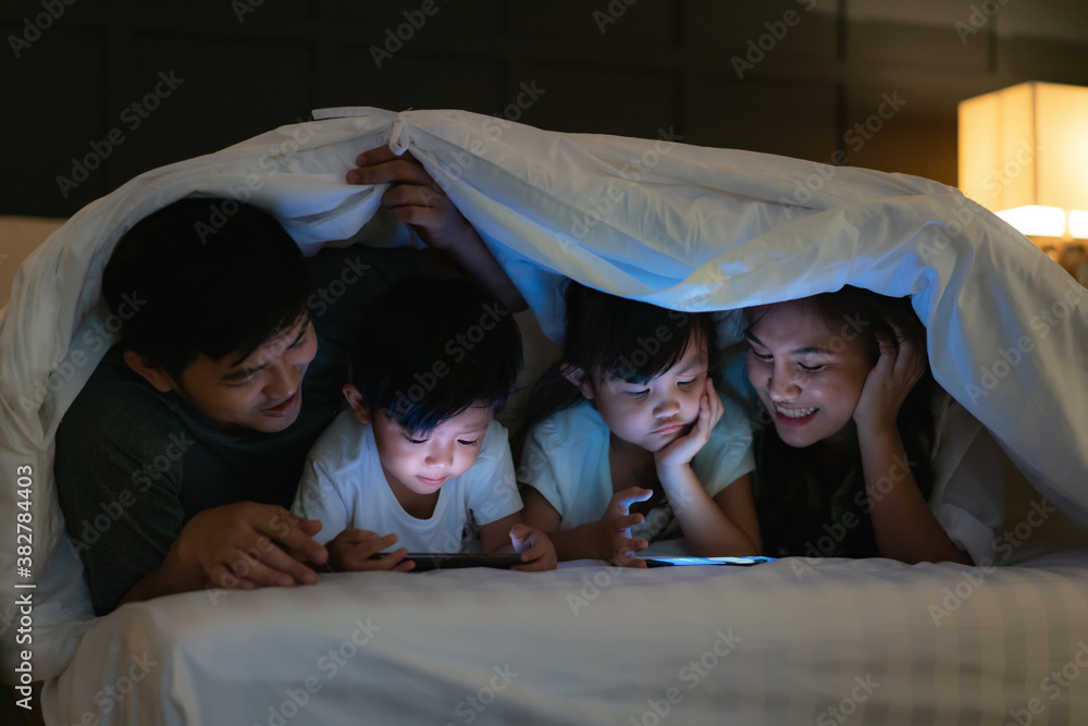 Asian happy family mother, father and little daughter and son watching movie or cartoon in smartphon