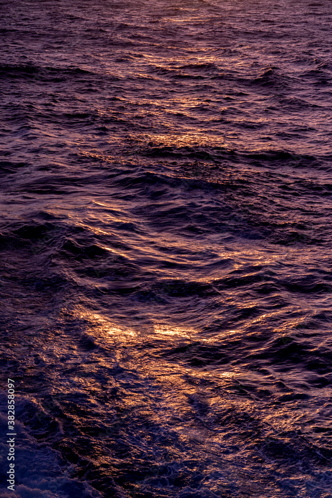 Golden evening sunlight reflecting in the moving wave water, texture close-up. Summer sunset moment