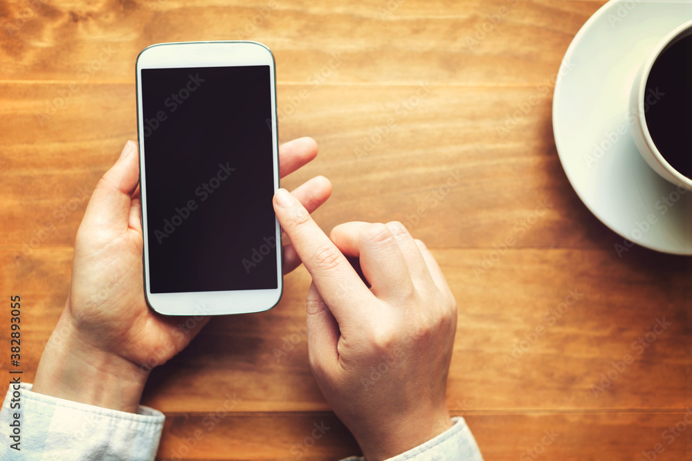 Person using a white smartphone on a wooden table