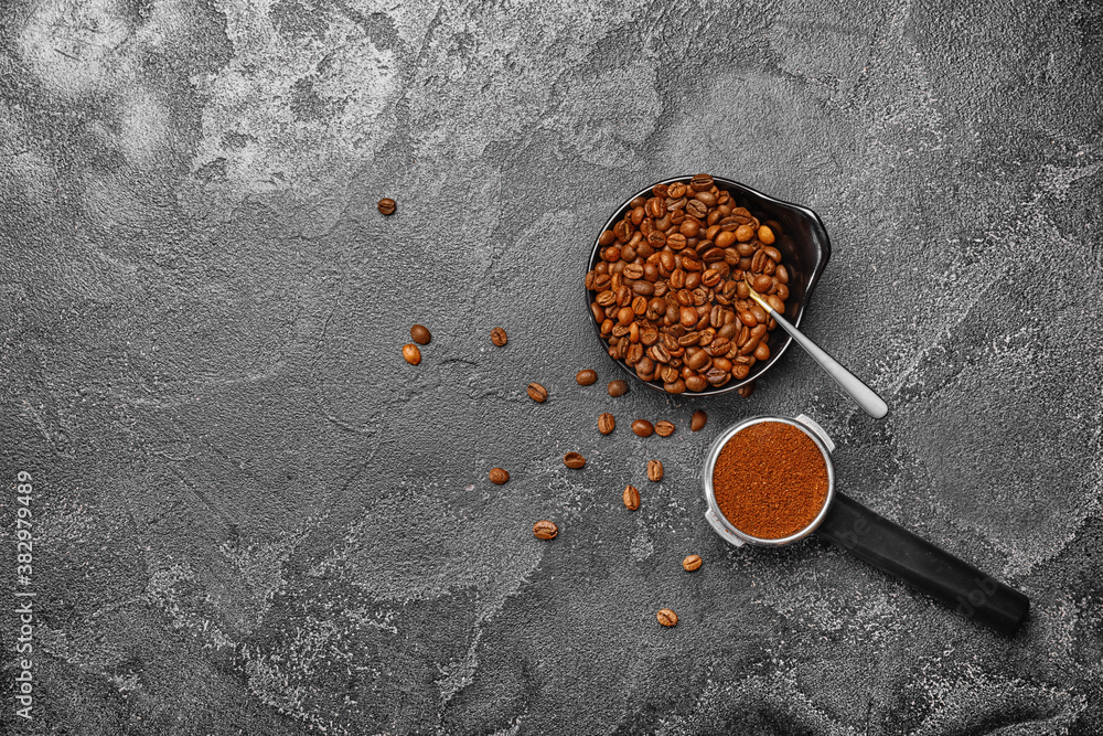 Portafilter with coffee powder and beans in bowl on dark background