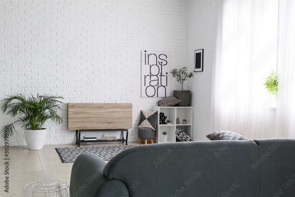 Stylish interior of room with wooden stand near white brick wall