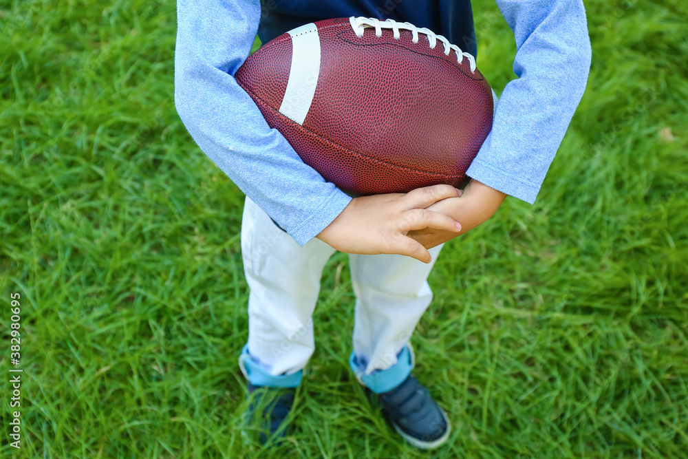 Little boy playing American football outdoors