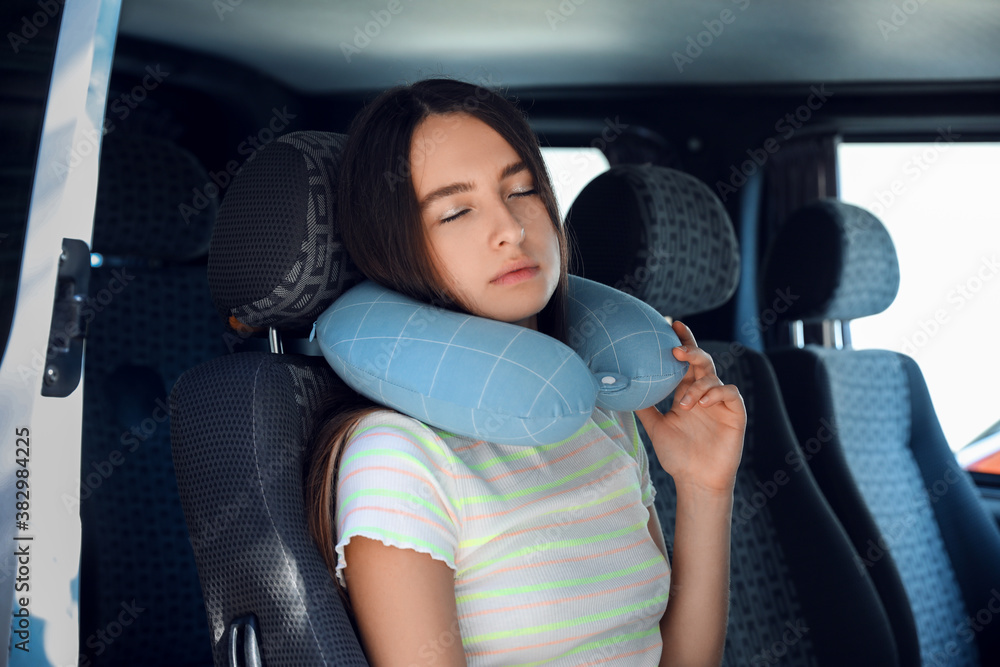 Beautiful young woman with travel pillow sitting in car