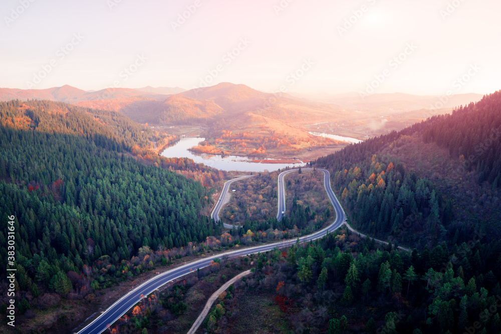 Aerial drone view over the autumn mountains with mountain road serpentine, river and forest. Landsca