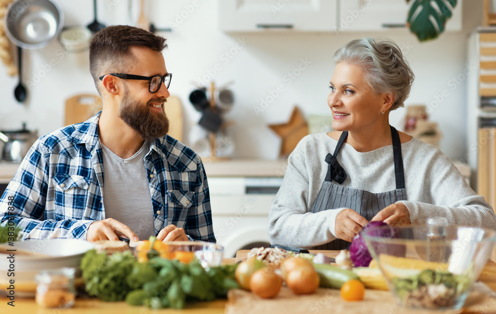 Happy mature woman with adult son cooking together at home.