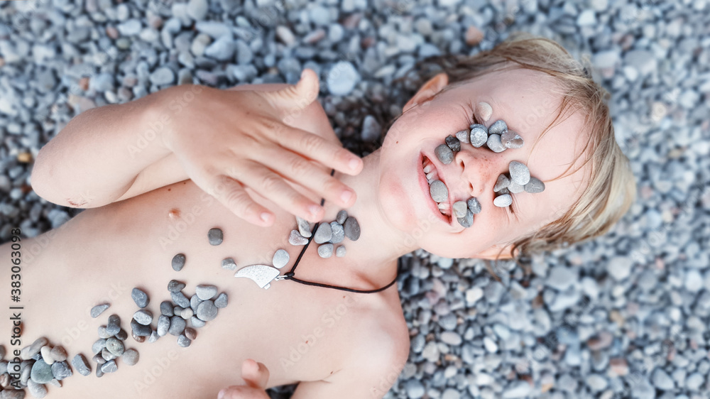 On sunny beach happy kids have fun, lying down on hot pebble, sunbathing, warming after swimming in 