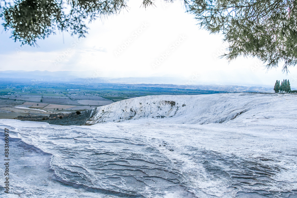 grey textured travertine hill under green trees with blue-white cloudy sky - Pamukkale