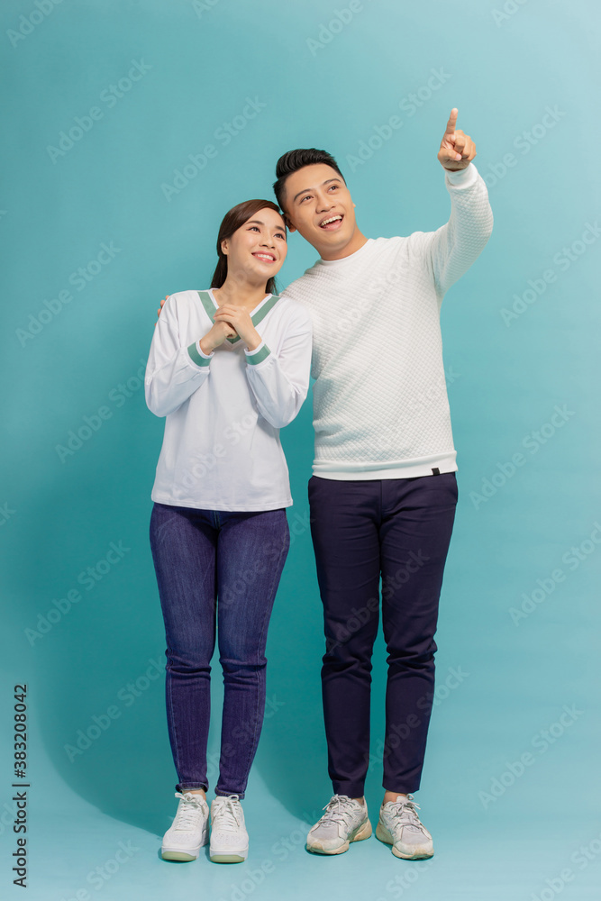 Young asian couple isolated on blue background pointing finger to the side