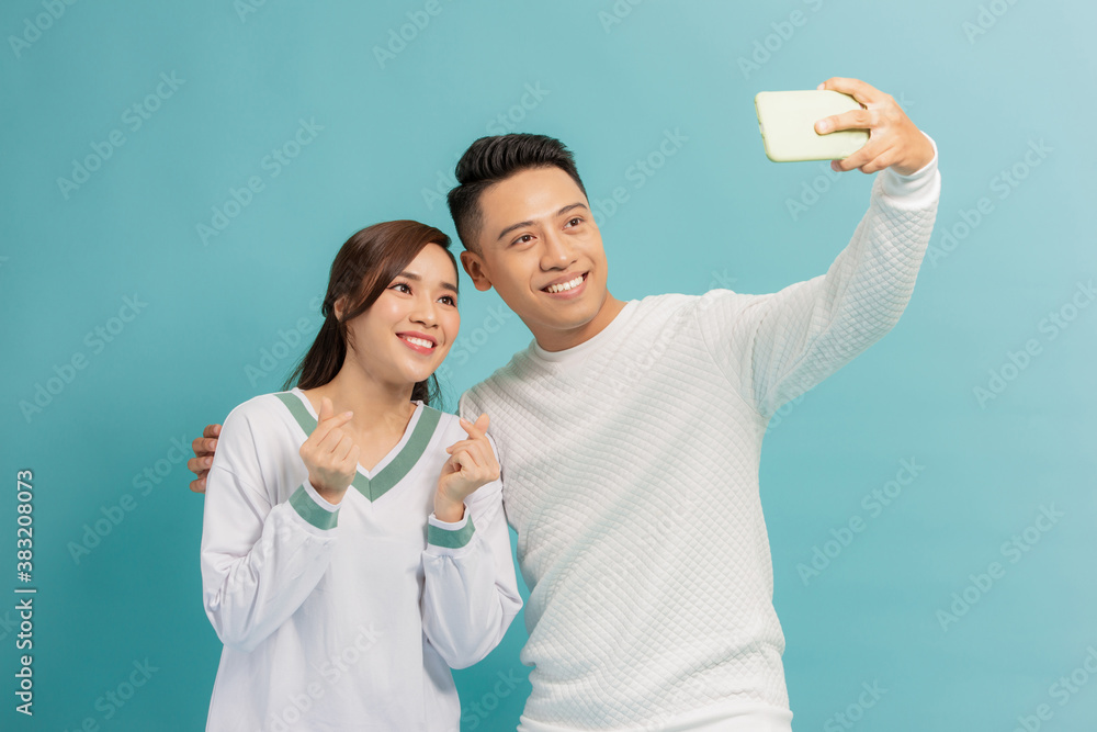 Happy young couple showing heart korean style while taking a selfie together isolated over blue back