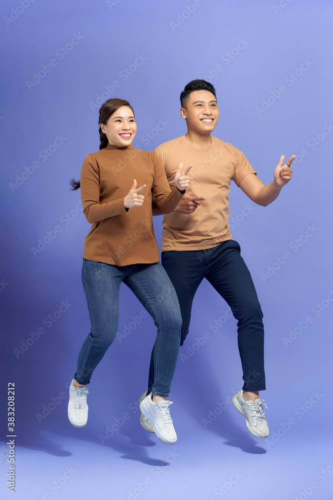 Energetic beautiful couple posing together on camera while running or jumping and pointing fingers o