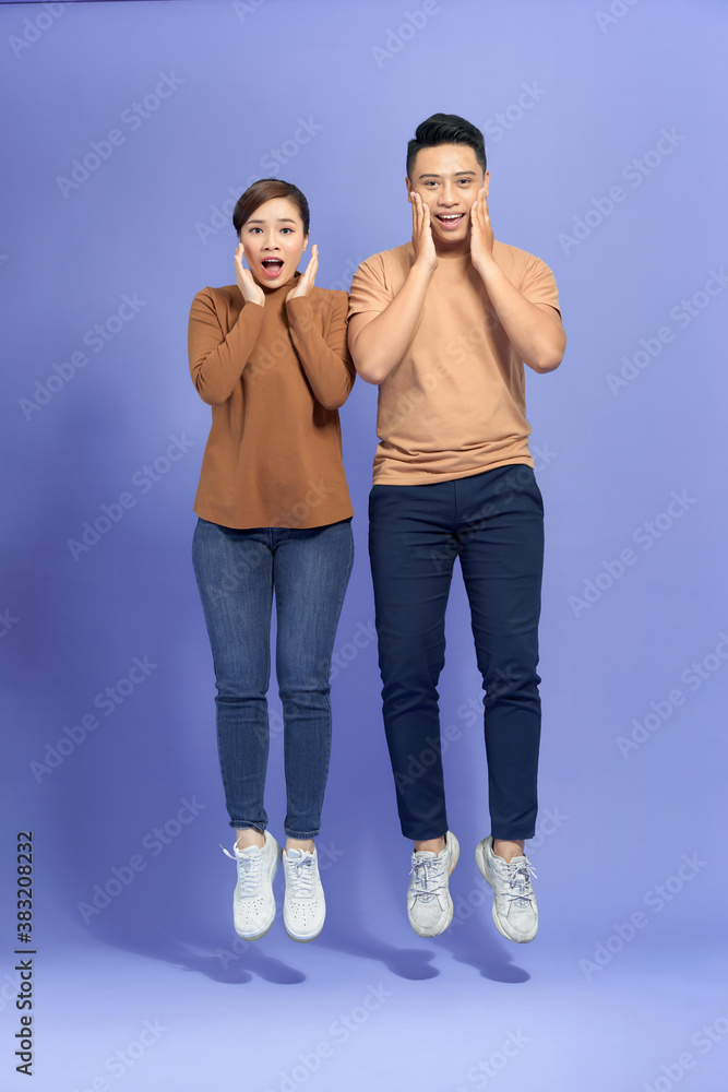 Young couple posing in a purple background celebrating a victory or success, he is surprised and sho